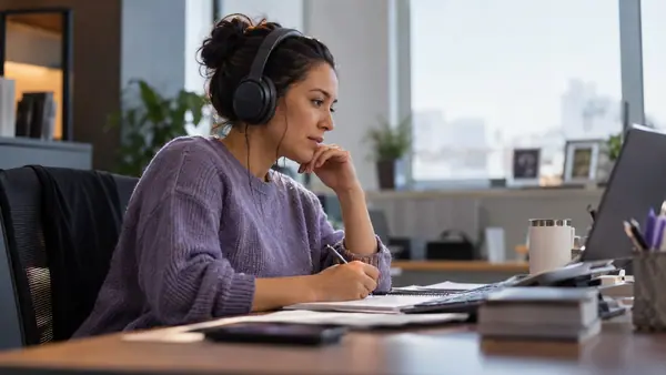 Quality supervisor listening through headphones while making review notes.