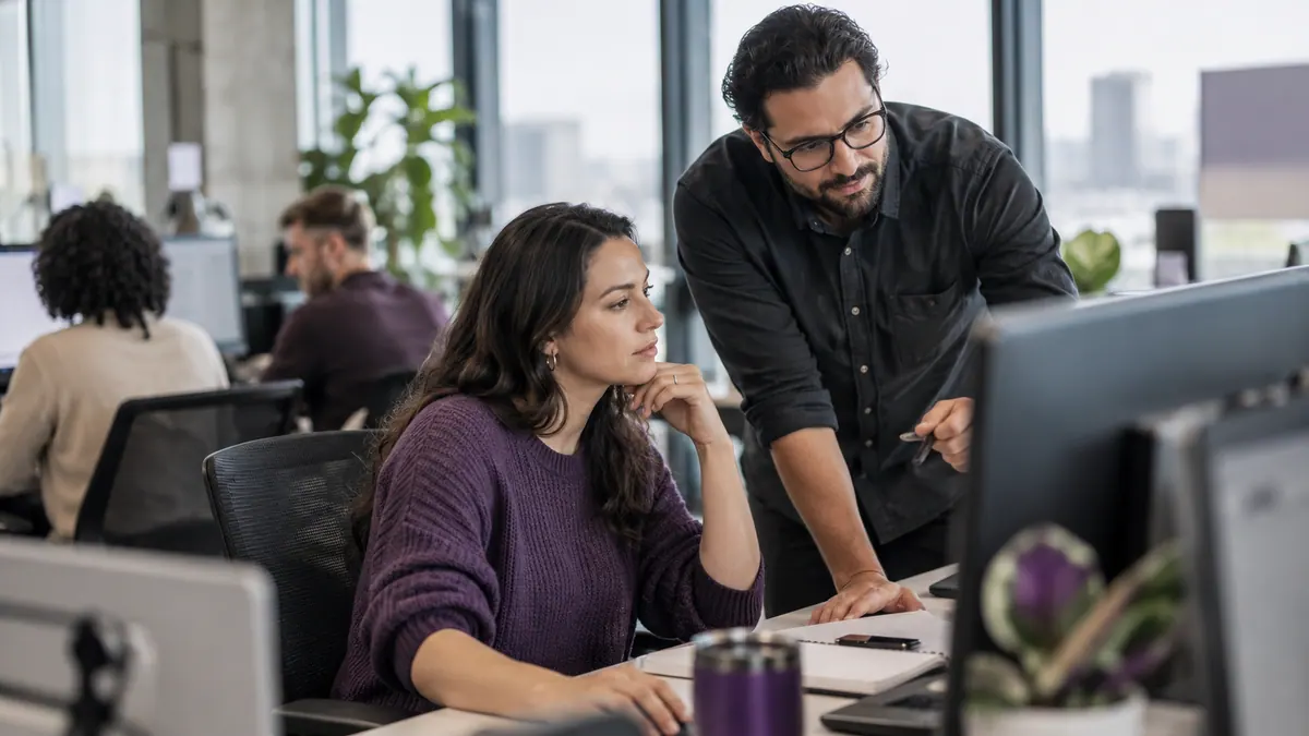 Customer service colleagues reviewing a support workstation in a daylight office.