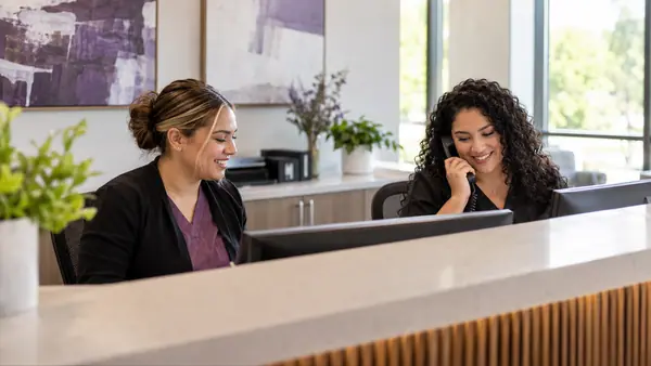 Non-clinical scheduling coordinators at an outpatient clinic reception desk.