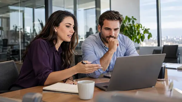 Sales colleagues discussing a business pipeline at a laptop in a meeting room.
